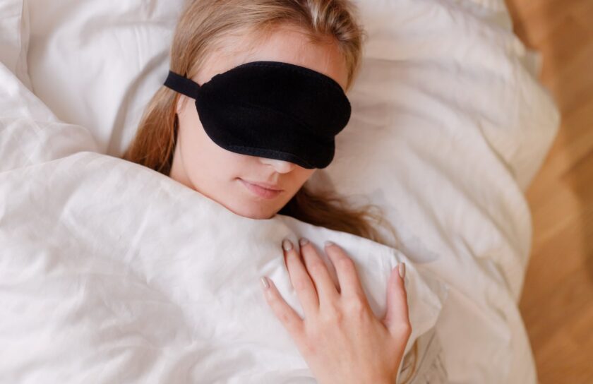 Sovende kvinde med sort sovemaske under hvid dyne