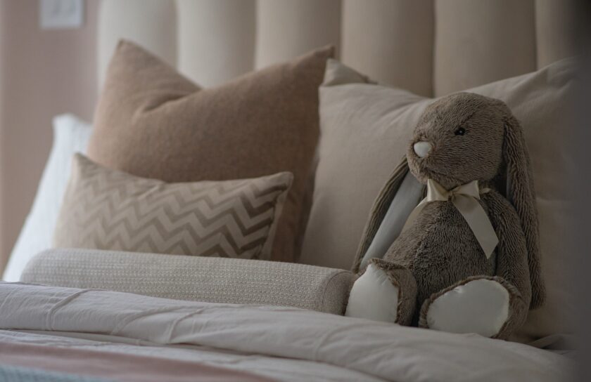 Hyggelig seng med bløde puder og en beige krammebamse kanin i rolige, neutrale toner