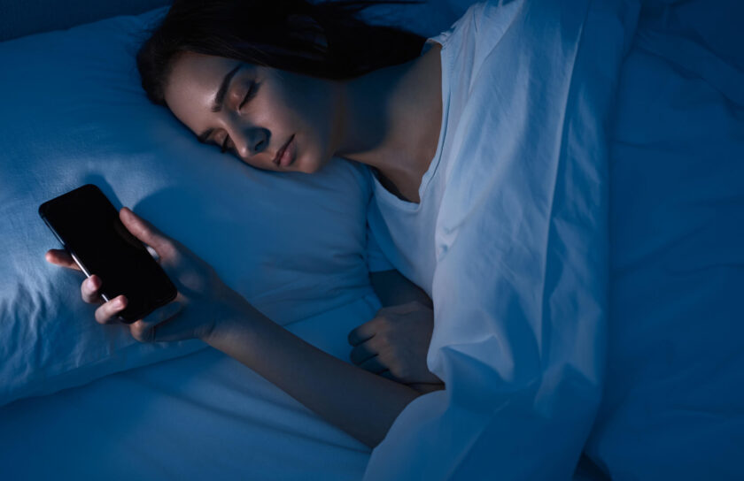 Sovende kvinde ligger med slukket smartphone i hånden under blåt nattelys