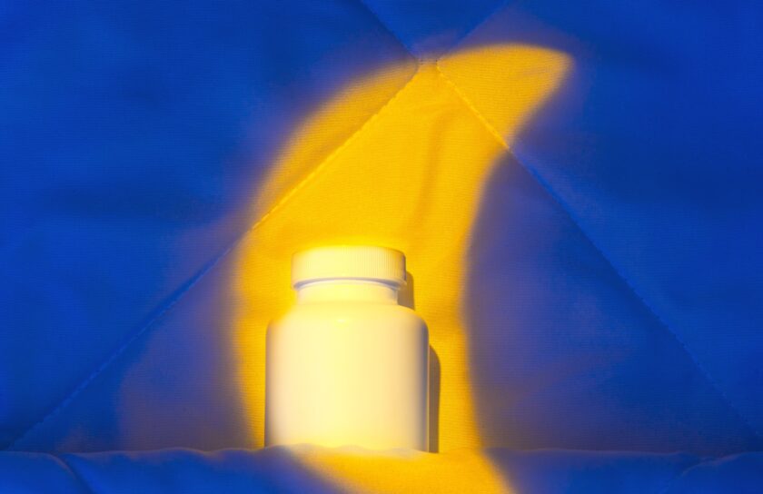 Hvid melatoninbeholder på dyne oplyst af varmt gult lys mod blå baggrund
