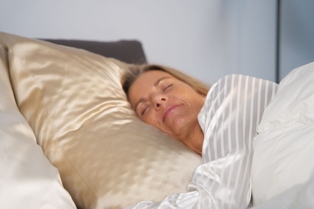 Kvinde sover fredeligt på glat gylden silkepude iført stribet pyjamas